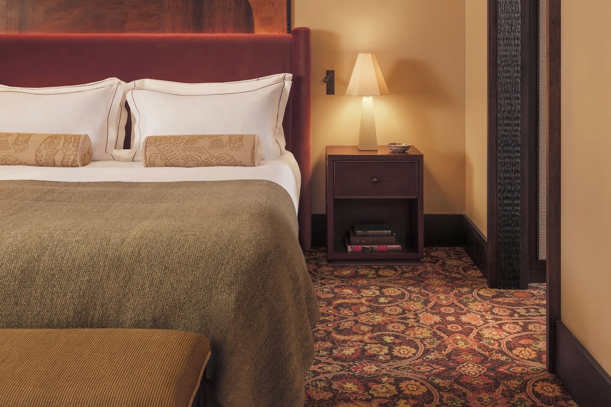 A hotel room with a large bed, a nightstand with a lamp, a patterned carpet, and a painting on the wall.