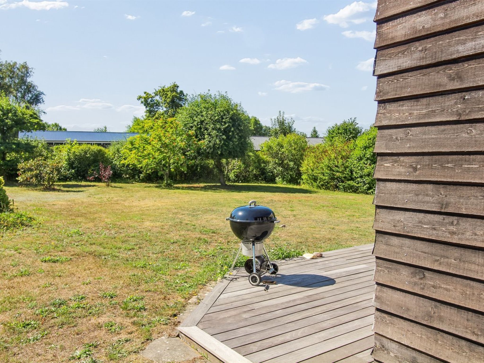Una griglia per barbecue su un patio di legno, con un prato e alberi sullo sfondo.