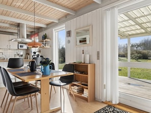 Eine moderne Küche mit Holzschränken, einem Essbereich mit Tisch und Stühlen und einem großen Fenster mit Blick ins Freie.