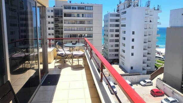 En balkon med rødt gelænder, et bord og to stole.