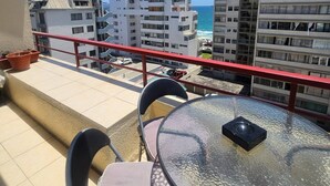 En balkon med et bord og stole, der ud til en strand og bygninger.