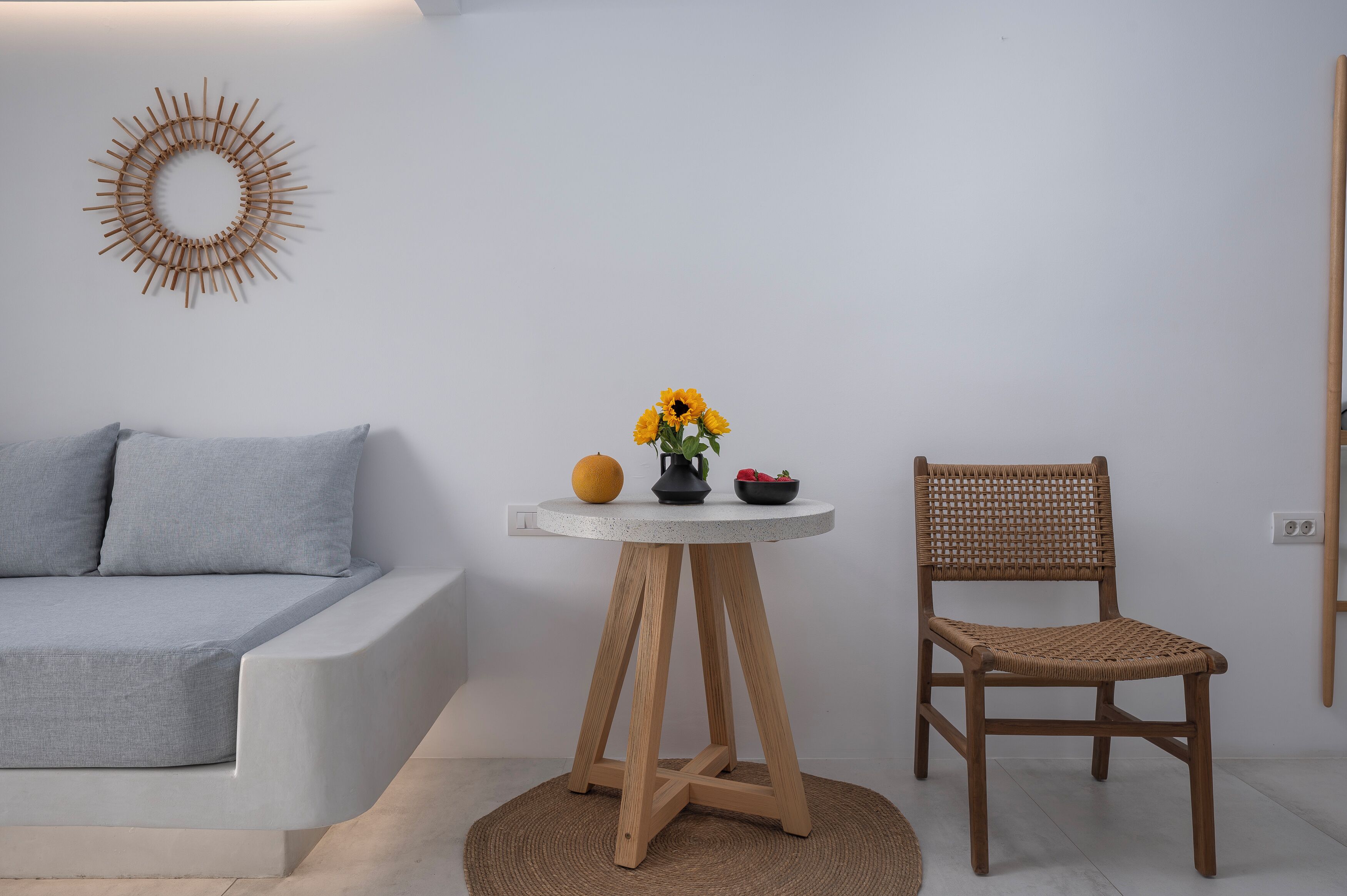 Una habitación moderna con un sofá gris, una mesa redonda de madera con un florero y una silla de mimbre.