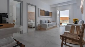 A modern living room with a sofa, a coffee table, and a chair. There is a television mounted on the wall and a small stool. - Ios Art Suites (Ios)