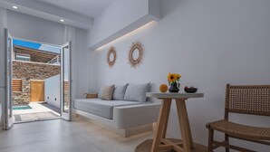 A modern living room with a sofa, a small table with a vase, and a wicker chair. - Ios Art Suites (Ios)