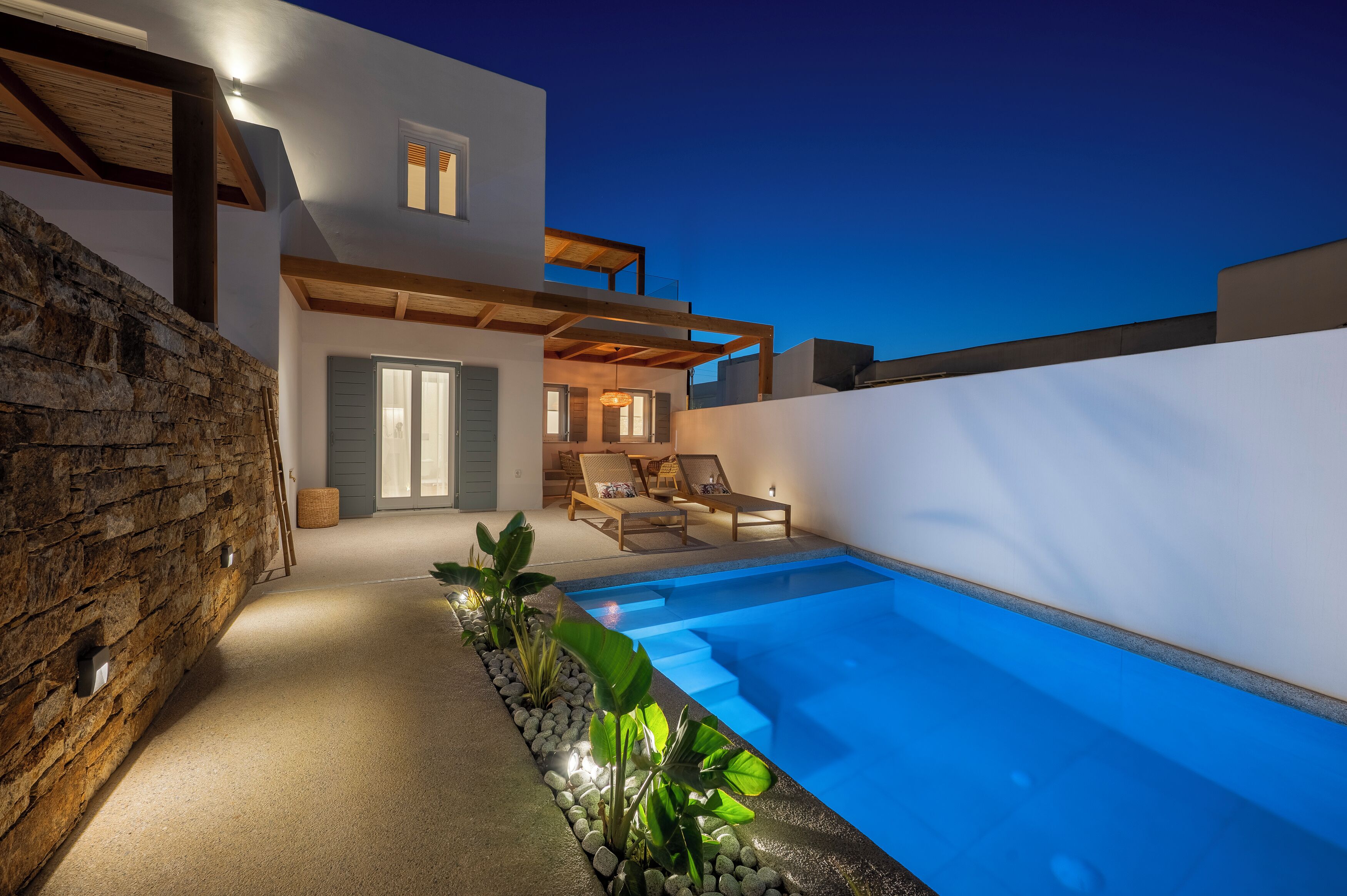 A modern house with a swimming pool, stone wall, and a cozy seating area with a view of the pool.