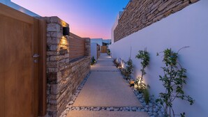 A narrow pathway flanked by stone walls and a wooden door, leading to a building with a stone facade. - Ios Art Suites (Ios)