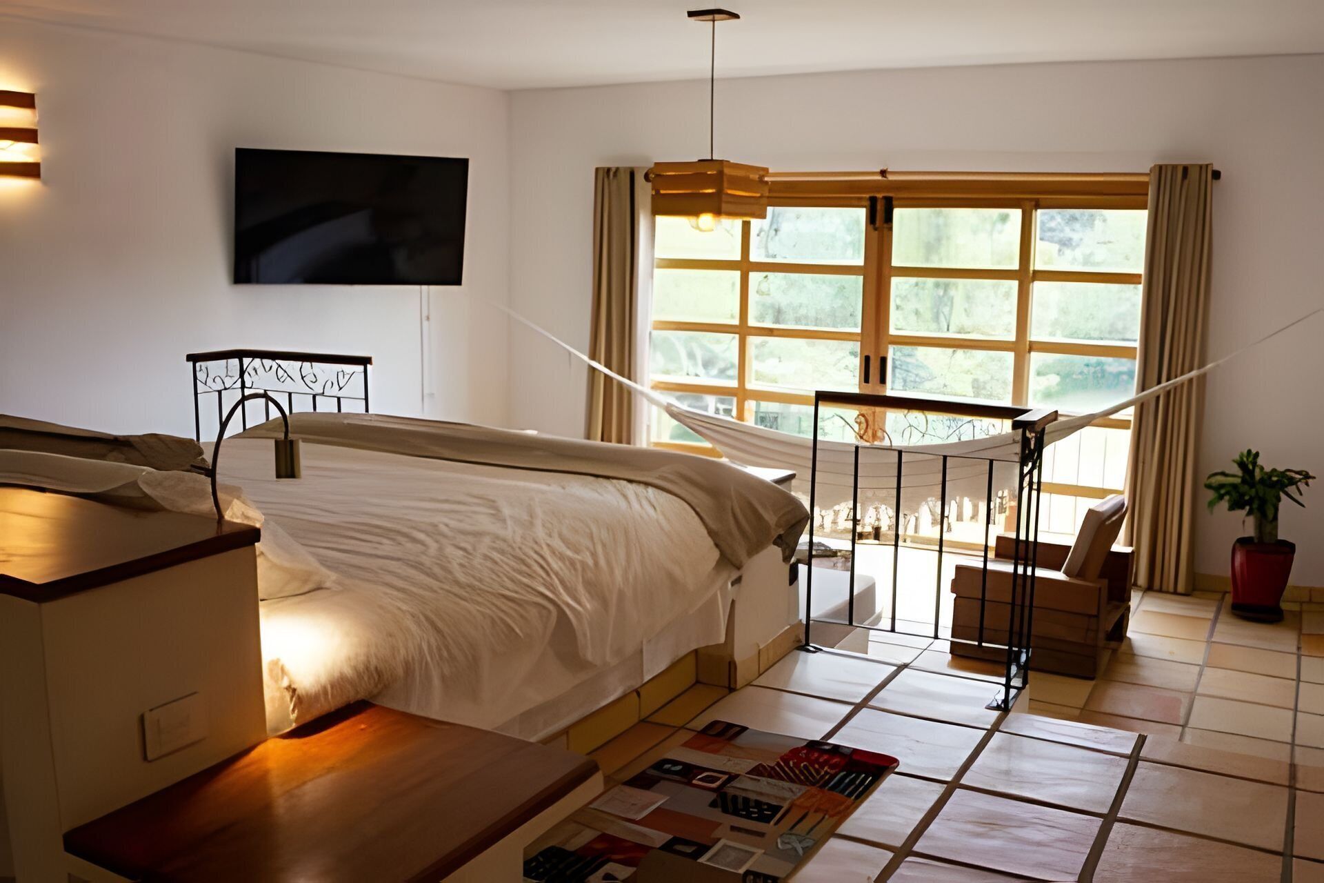 Un dormitorio con cama, televisión, hamaca, ventana y planta en maceta.