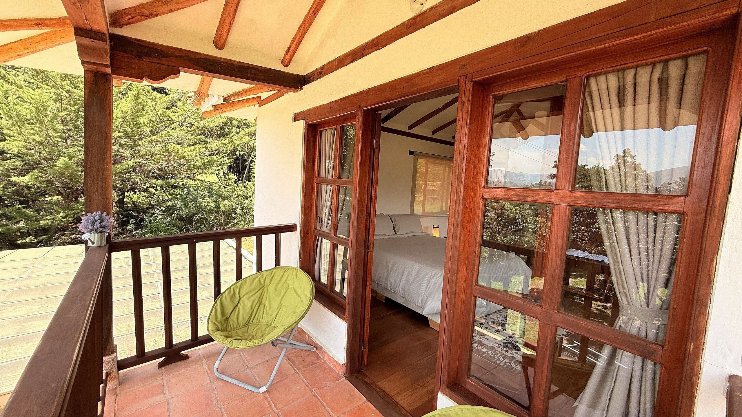 A balcony with a wooden railing, a green chair, and a bed visible through a large window.