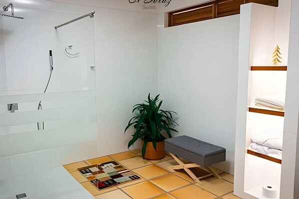A modern bathroom with a shower, a bench, a potted plant, and a shelf with towels. - El Solaz By Honnor Living   (Villa de Leyva)