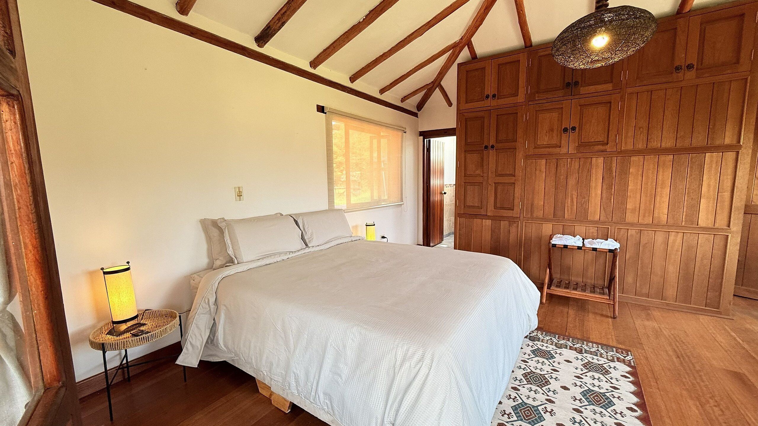 A bedroom with a large bed, wooden wardrobe, and a hanging light fixture.
