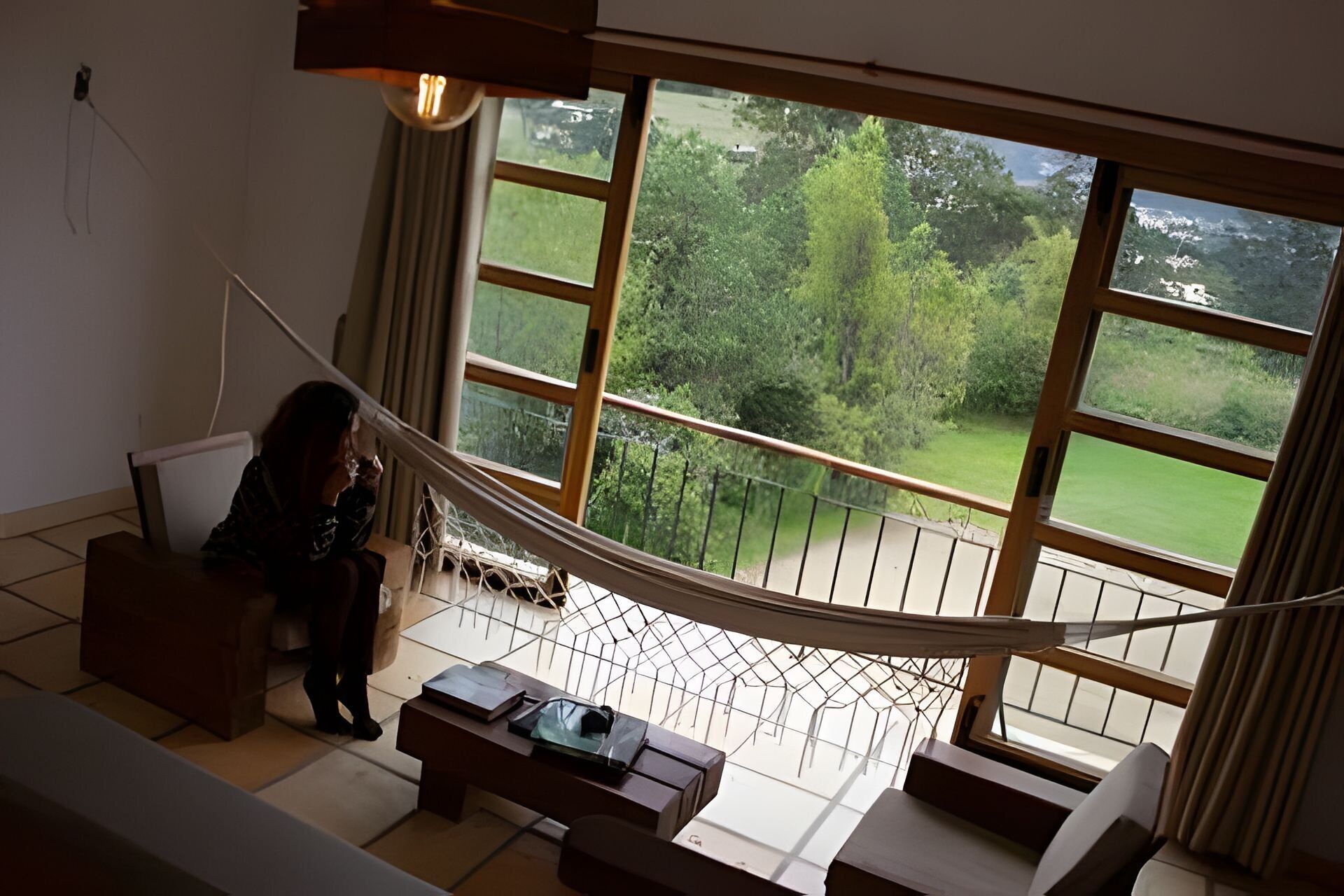 Una habitación con un ventanal grande, una hamaca y vistas a un paisaje verde.