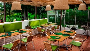 Un restaurante con terraza, sillas acolchadas verdes y mesas de madera.