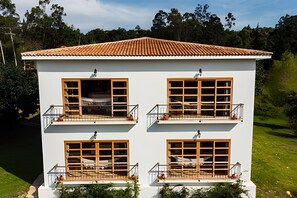 Un edificio de dos plantas con tejado de tejas, varios balcones con barandillas y ventanas amplias.