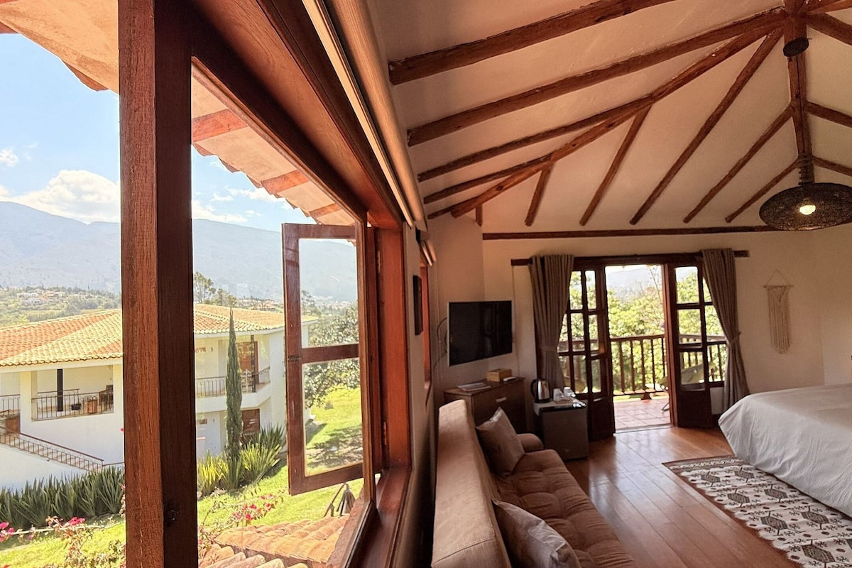 A bedroom with a large bed, a sofa, a TV, and a view of a mountainous landscape.