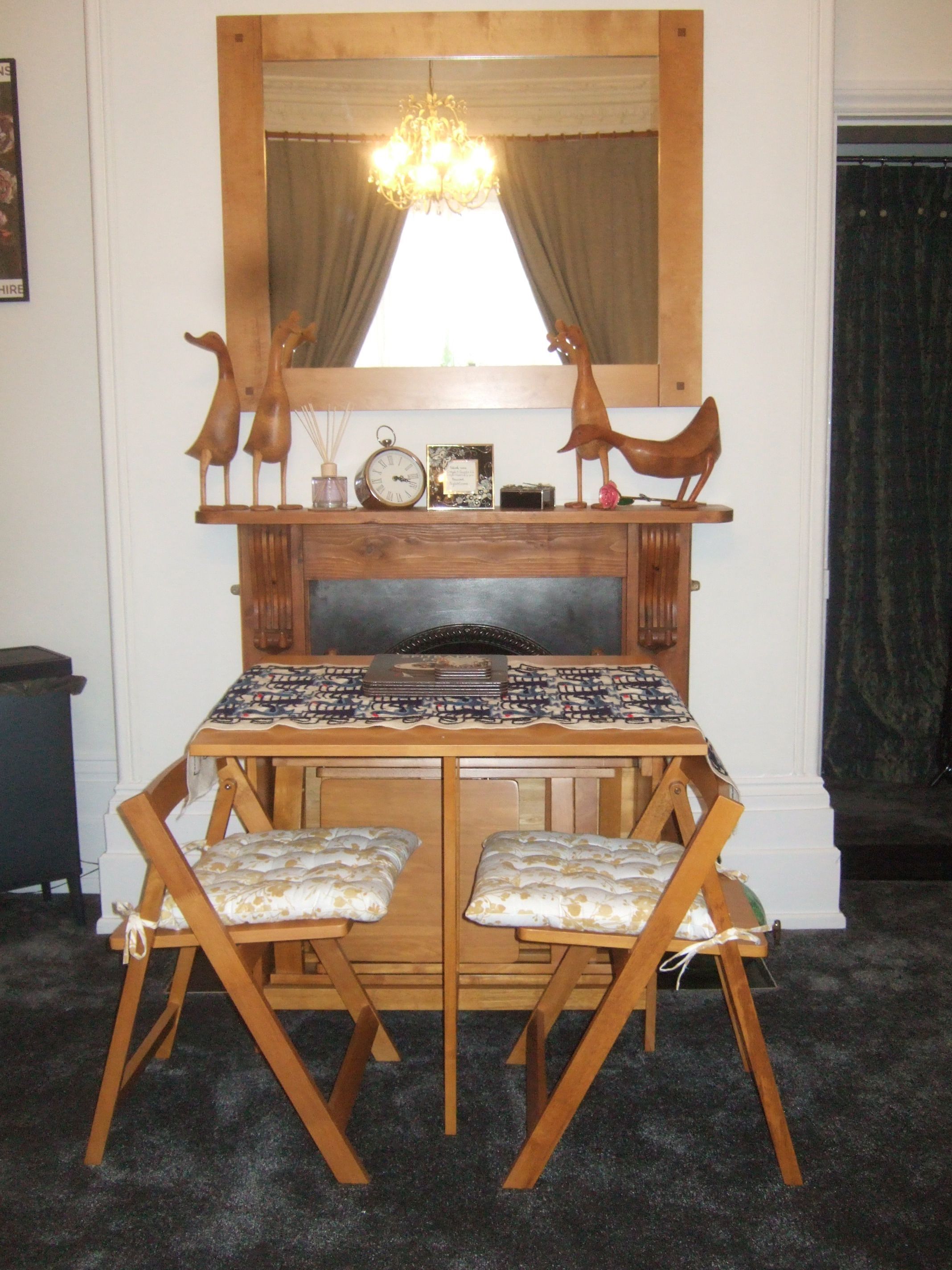 A dining table with two wooden chairs, a chandelier, and a mirror above the table.