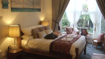 A bedroom with a bed, bedside lamps, a window with curtains, and a view of greenery outside.