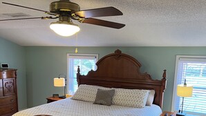 A bedroom with a wooden bed, a ceiling fan, two bedside tables with lamps, and a dresser.