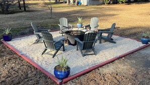 A patio area with four Adirondack chairs arranged around a circular table, surrounded by a gravel border.