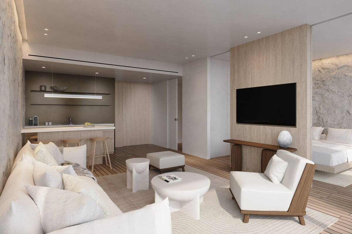 A modern living room with a sofa, ottomans, a coffee table, a TV, and a kitchen area with a bar.