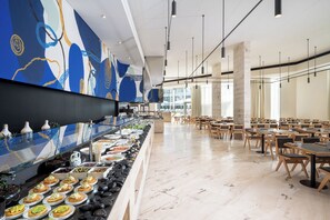 A buffet with various food items, a seating area with tables and chairs, and a large abstract mural on the wall.