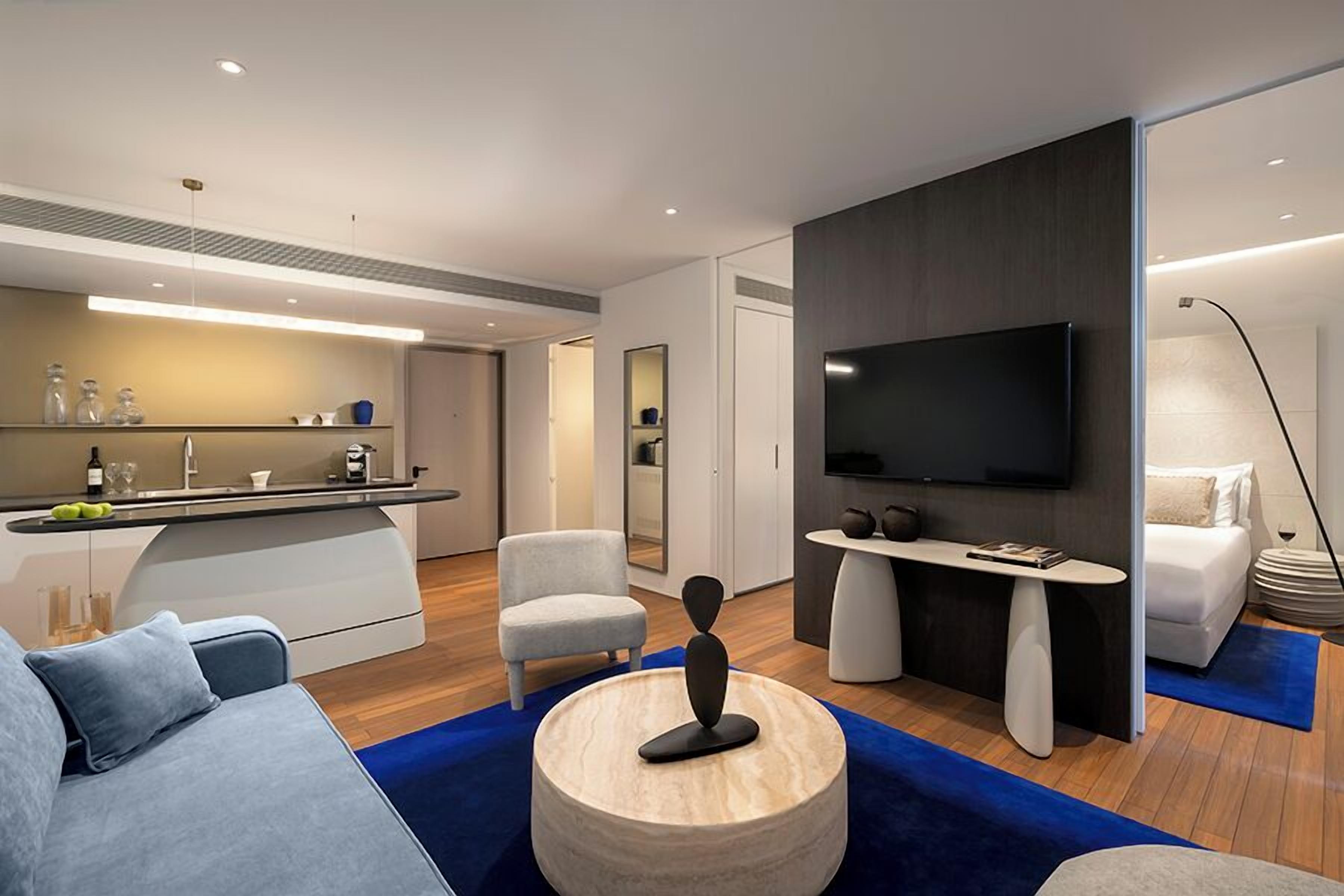 A modern living room with a sofa, a coffee table, a TV, and a kitchen area.