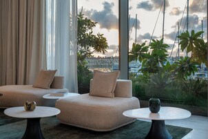 A modern living area with a sofa, two round tables, and a view of boats and greenery.