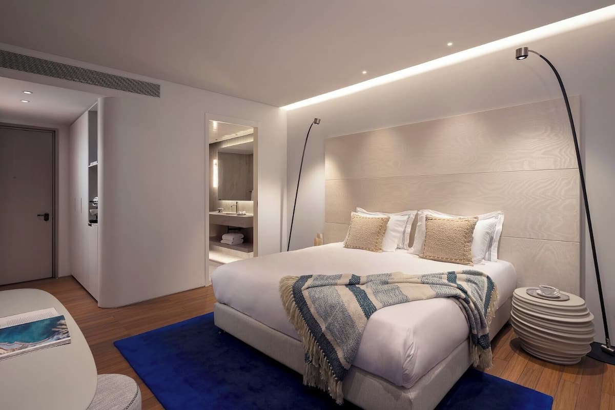 A modern bedroom with a large bed, bedside tables, a built-in wardrobe, and a bathroom with a vanity.