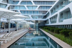 A modern building with a pool, sun loungers, and umbrellas.