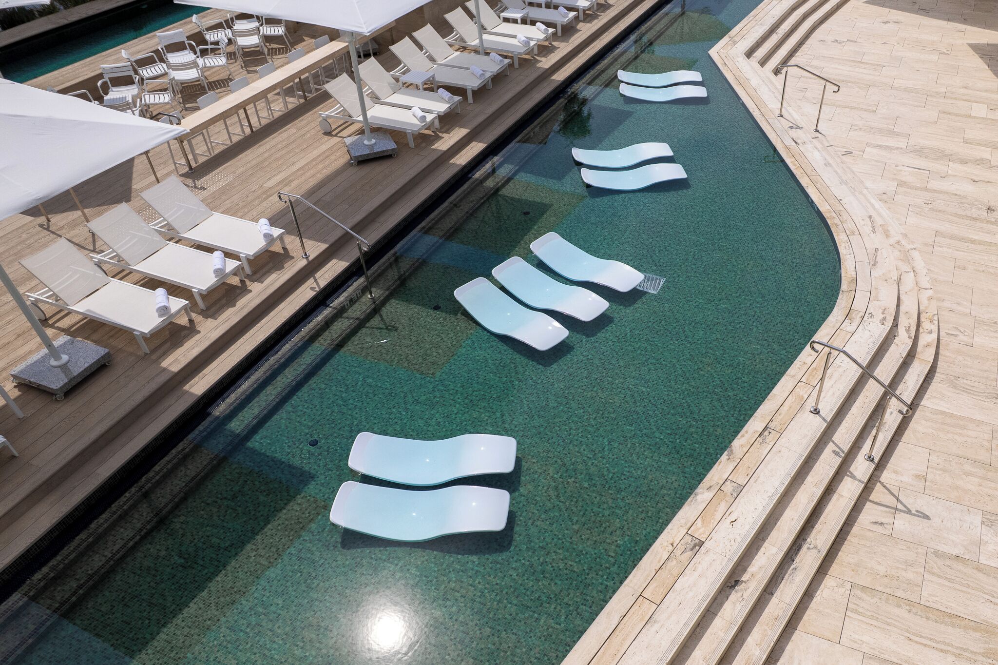 A pool area with lounge chairs and sun loungers, a wooden deck, and a clear blue pool.