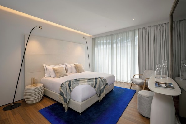 Un dormitorio moderno con una cama grande, lámparas de noche, una mesita con vasos y una silla.