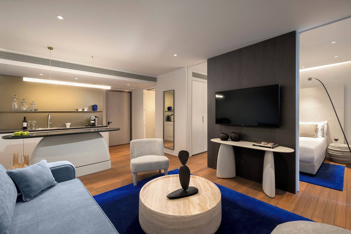 A modern living room with a sofa, a coffee table, a TV, and a kitchen area with a counter and cabinets.