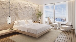 A modern bedroom with a bed, a side table, a chair, and a view of a marina through large windows. - The YACHT – Limited Edition By Fattal (Herzliya)