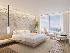 A modern bedroom with a bed, a side table, a chair, and a view of a marina through large windows.