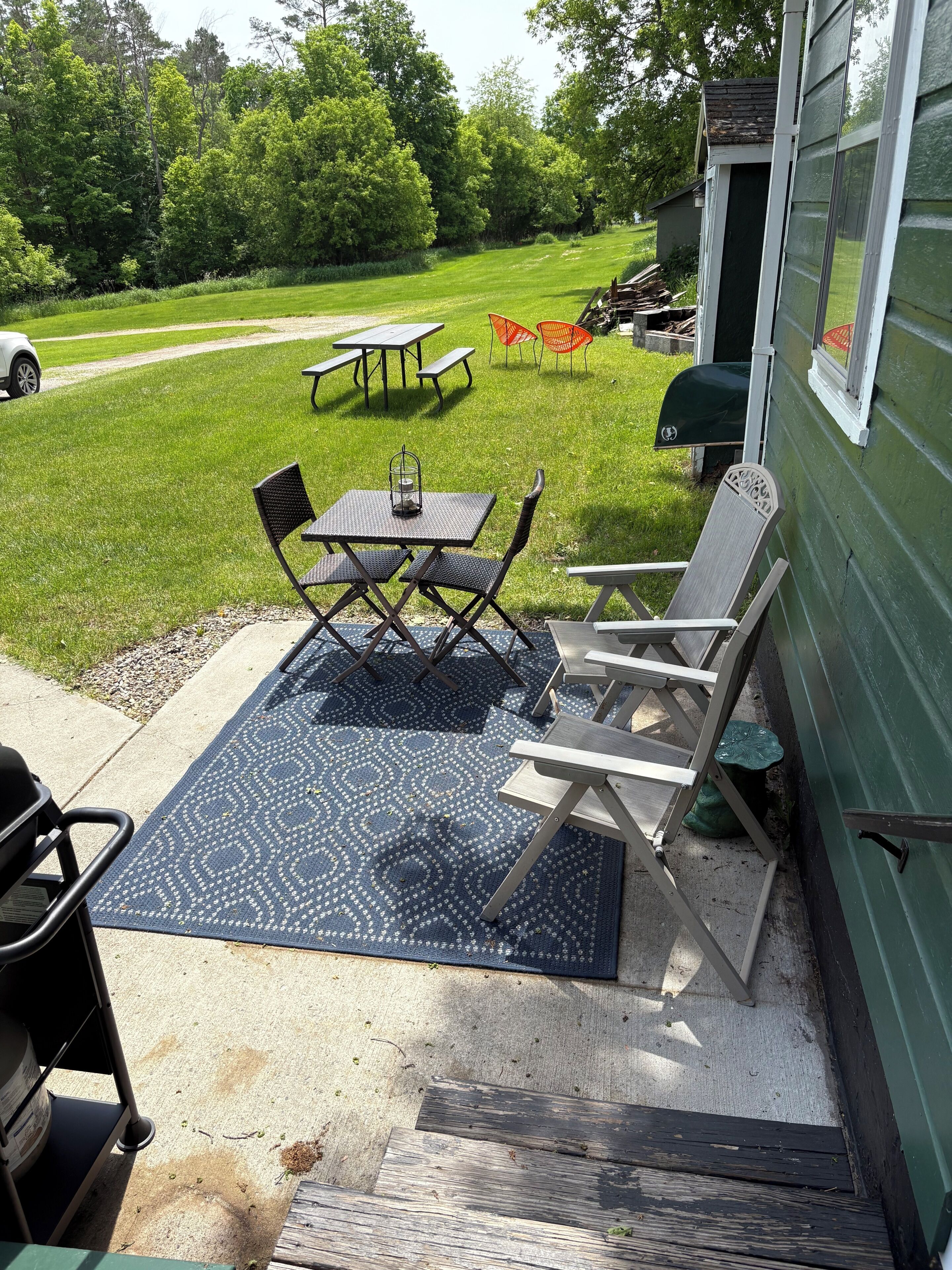 En terrasse med udendørs møbler, grill og et drivhus i baggrunden.