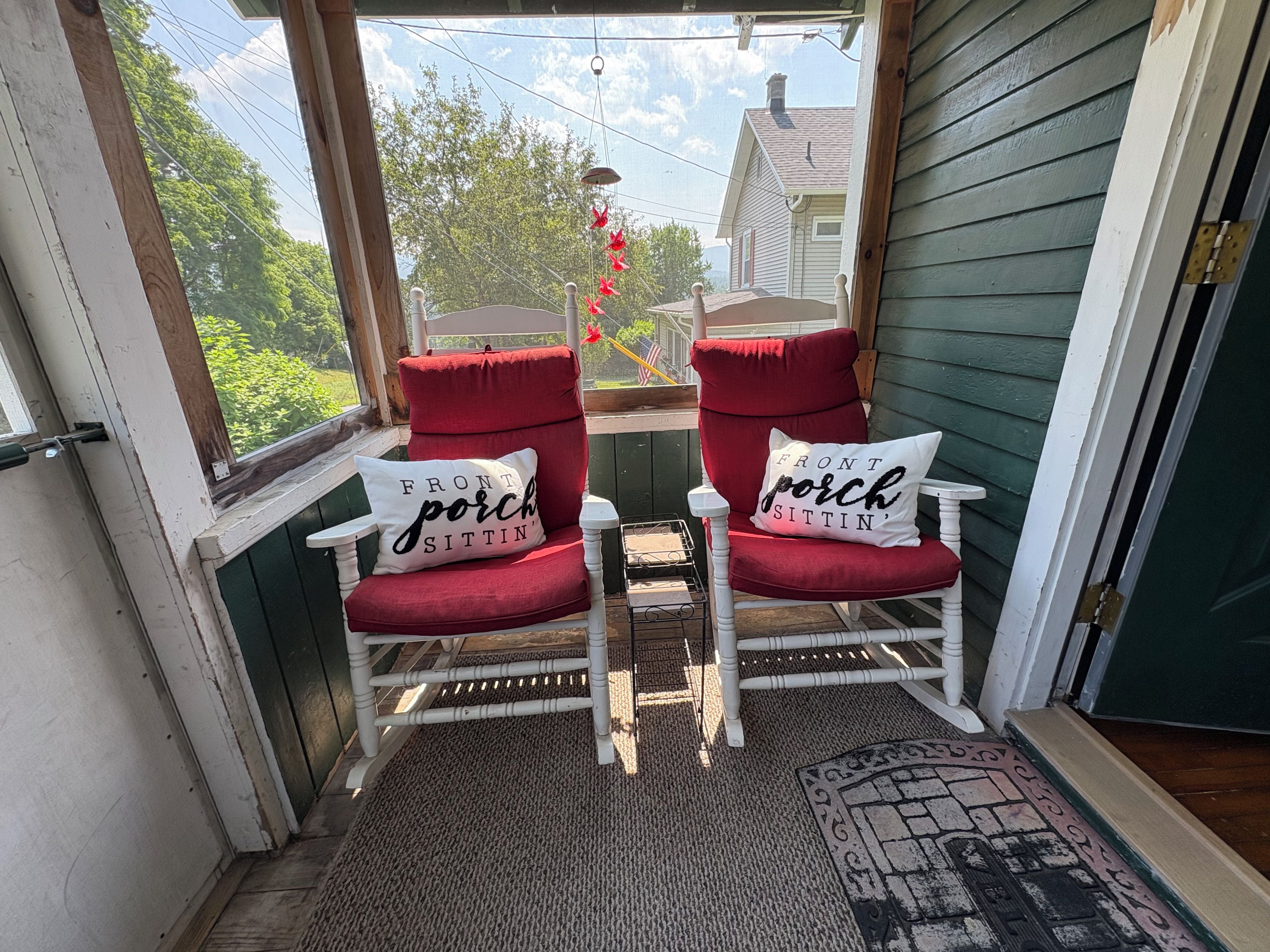 Un porche con dos sillones tapizados en rojo y cojines a juego, una mesita y vistas a una casa y árboles.