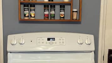 A white stove with four burners and a digital clock displaying 3:57. Above the stove, there is a wooden spice rack with various seasonings.