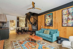 A modern living room with a teal sofa, a wooden ceiling fan, and a colorful rug. - Luxury family Duplex, 4 bdrs 10P - Republique (Paris)