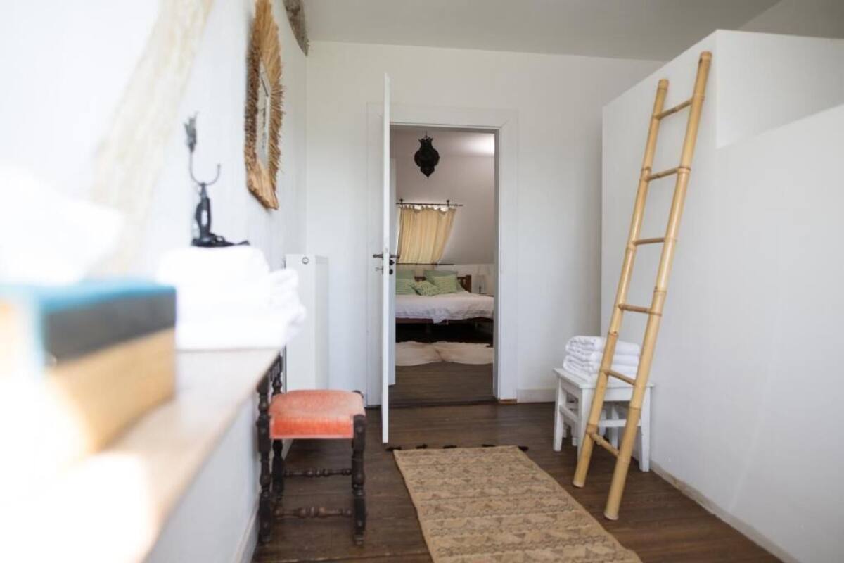A narrow hallway with a wooden bench, a ladder, and a bed in the adjacent room.