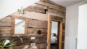 Een rustieke badkamer met een houten wand, een grote spiegel, een stenen wastafel en een deur naar een andere kamer.