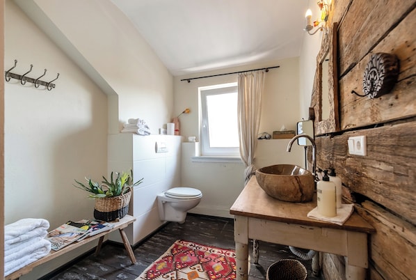 A bathroom with a wooden vanity, a sink, a toilet, a window with curtains, a shelf with toiletries, and a plant on a shelf. - Kaffee&Kissen - Boutique Hotel a. Rhein (Oestrich-Winkel)