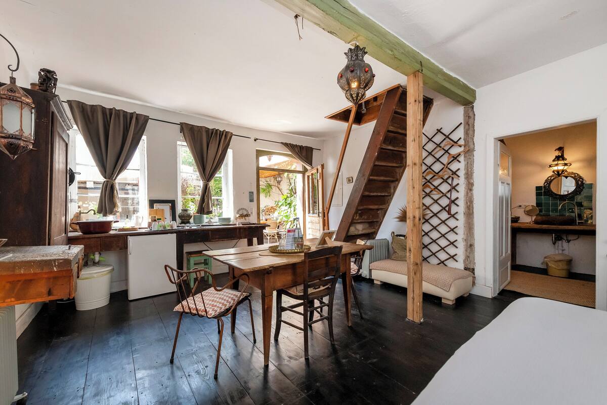 A rustic kitchen with a wooden table, chairs, and a staircase leading to an upper level.