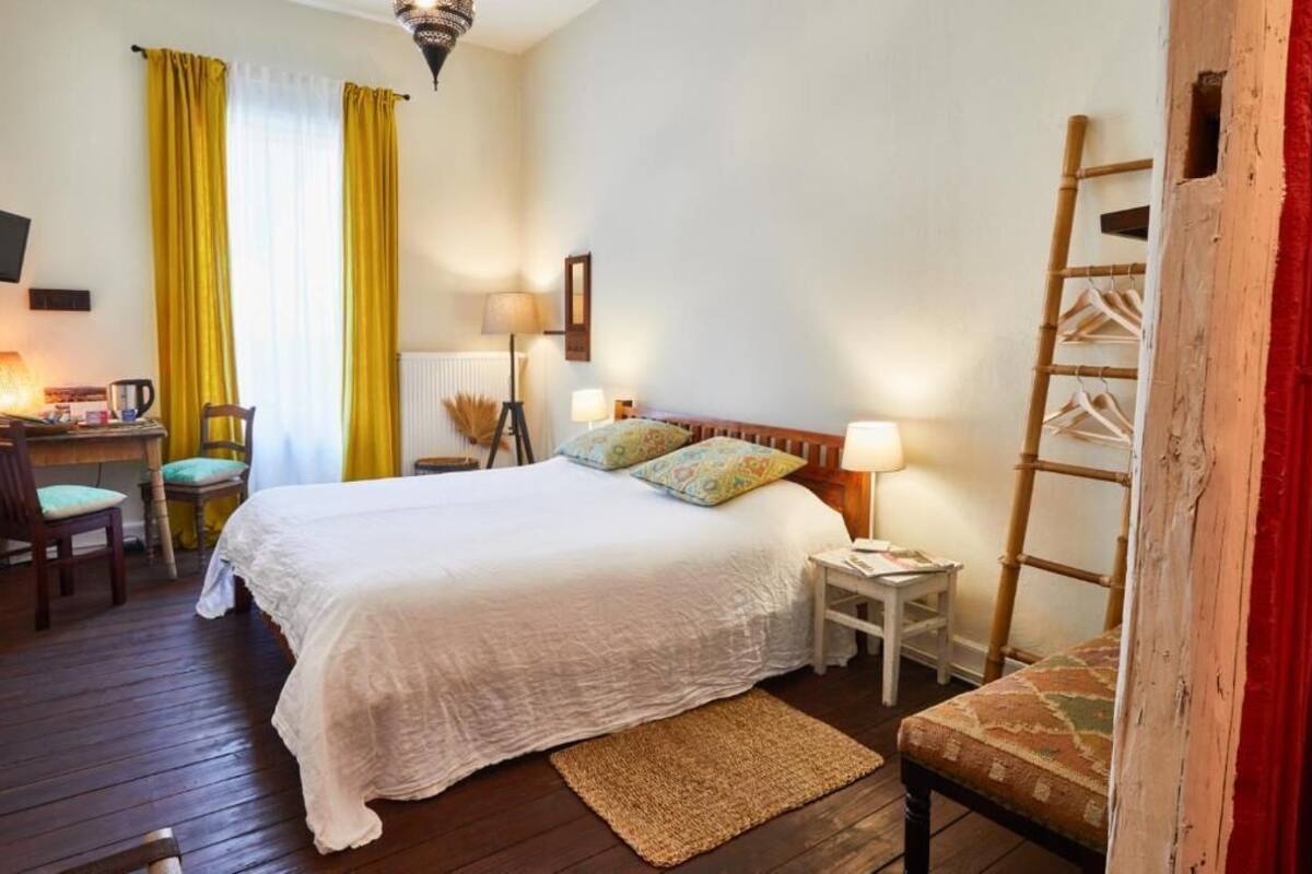 A bedroom with a large bed, bedside tables, a chair, a desk, and a ladder against the wall.