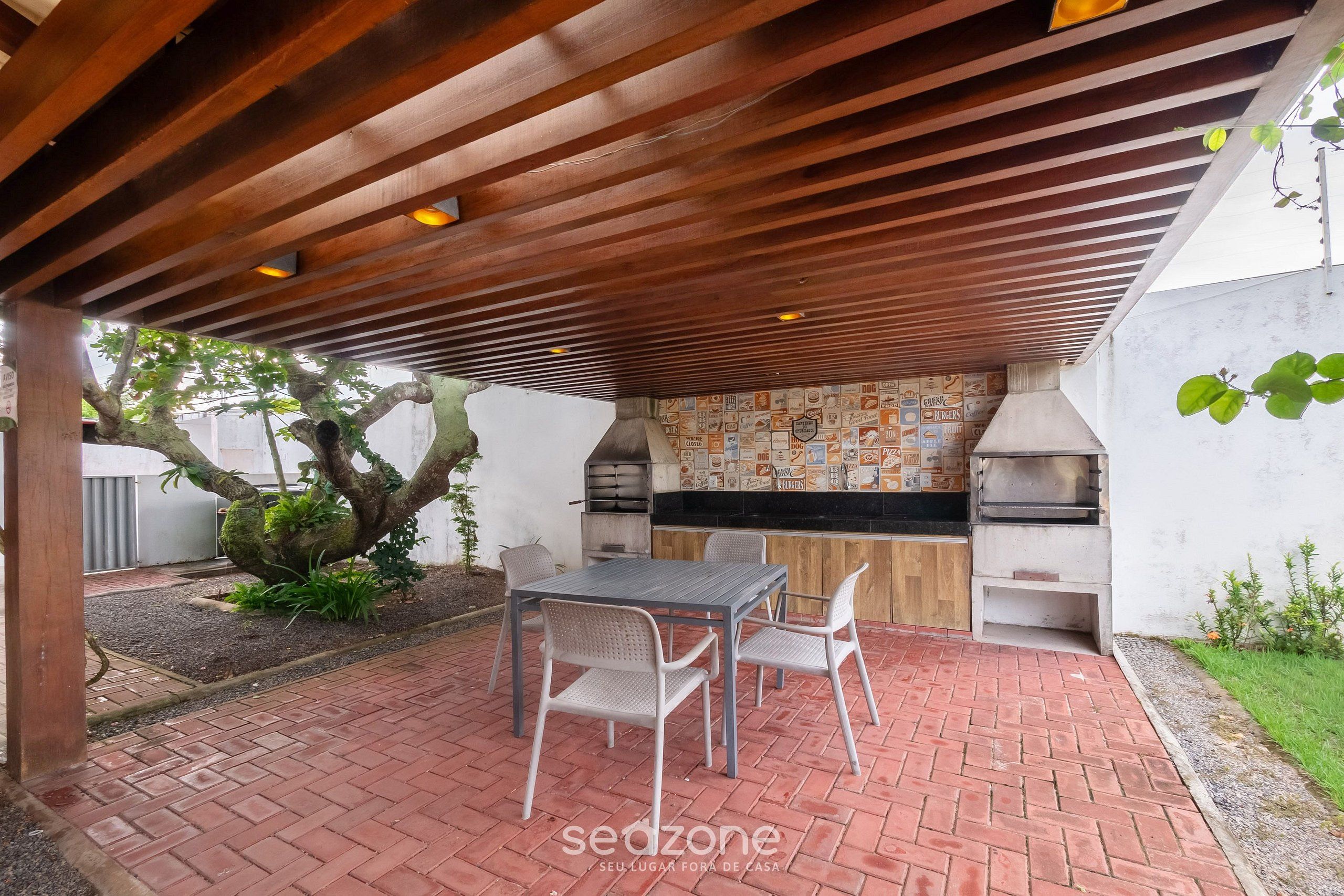 An outdoor patio with a brick floor, a wooden pergola, a table with chairs, and a built-in grill area.