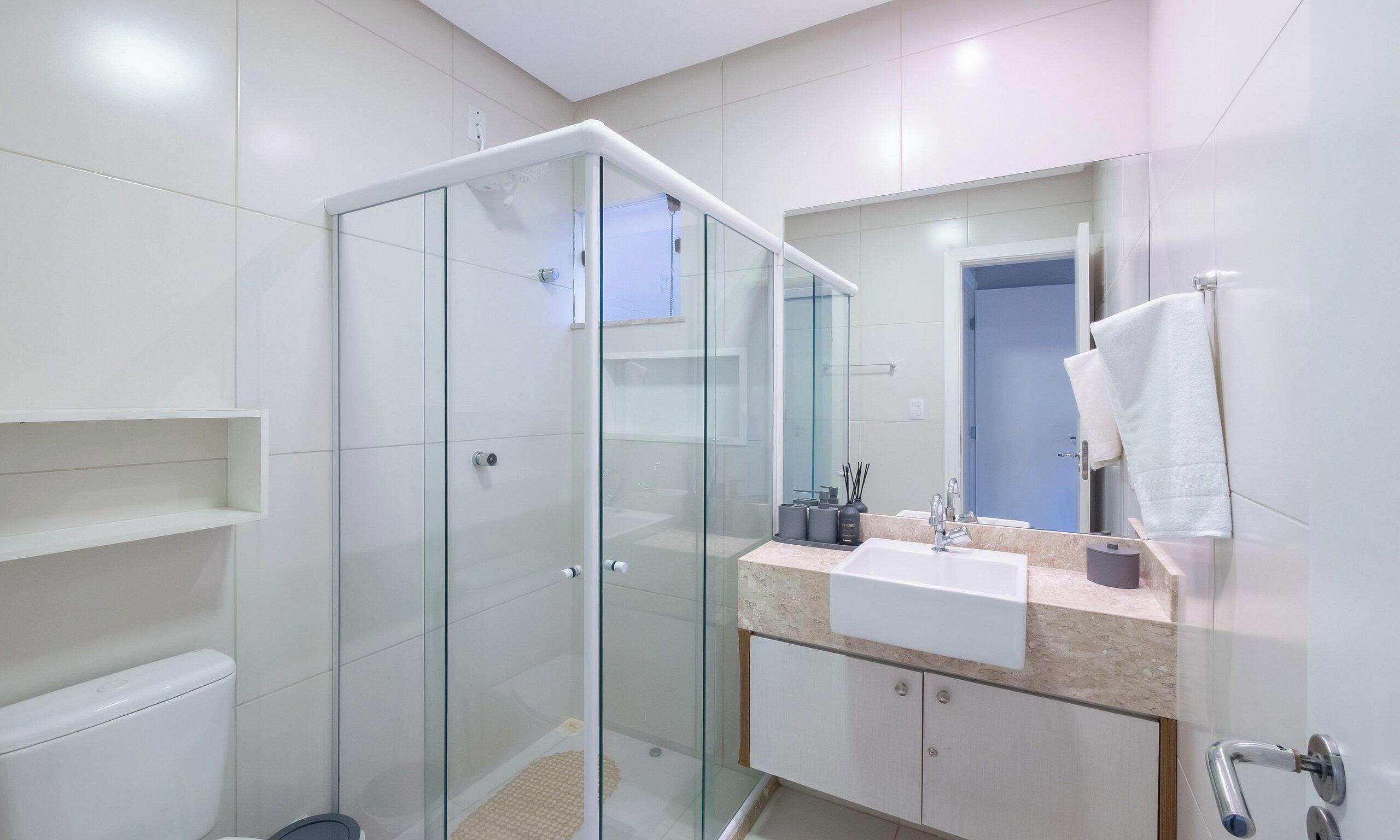 Un baño moderno con ducha envuelta en vidrio, un lavabo blanco y un espejo sobre él.