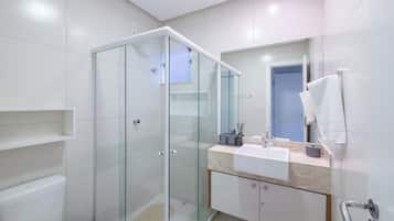 Un baño moderno con ducha envuelta en vidrio, un lavabo blanco y un espejo sobre él.