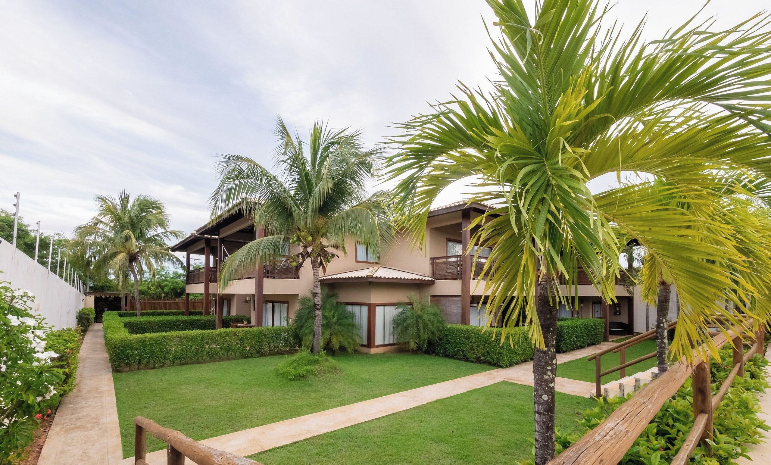 Un resort con edificios de varios pisos, un césped bien cuidado y palmeras.