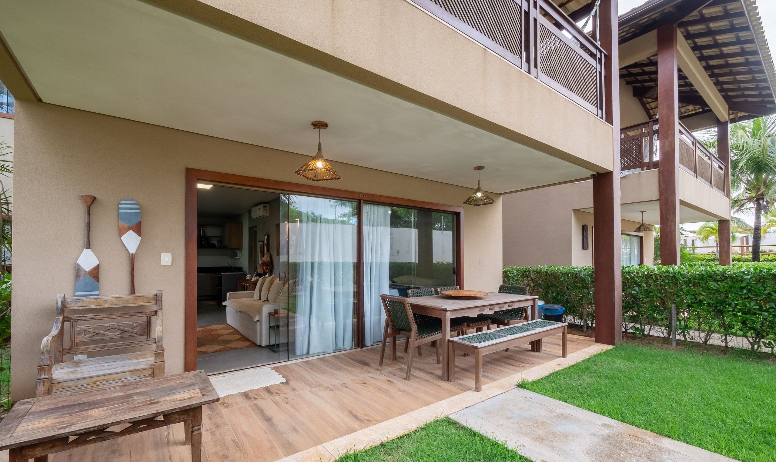 A covered outdoor seating area with a wooden table and chairs, a bench, and a view of the adjacent indoor space.