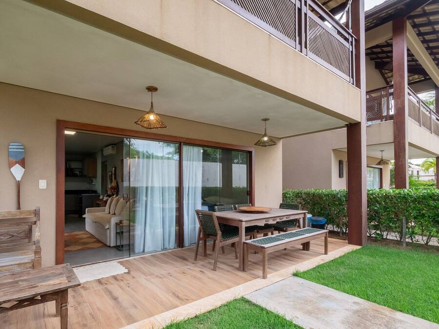 Un área de estar exterior cubierta con una mesa y sillas de madera, un banco y vistas al espacio interior contiguo.