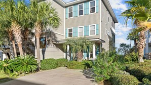 Un edificio residencial de varios pisos con fachada gris, contraventanas azules y un jardín cuidado con palmeras y arbustos.