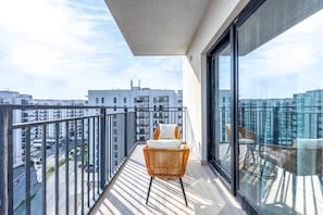 Un balcón con una silla de mimbre y cojines, con vistas a un paisaje urbano de edificios modernos.